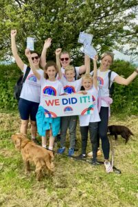 Three adults and three children hold a board saying 'WE DID IT' and cheer to the camera