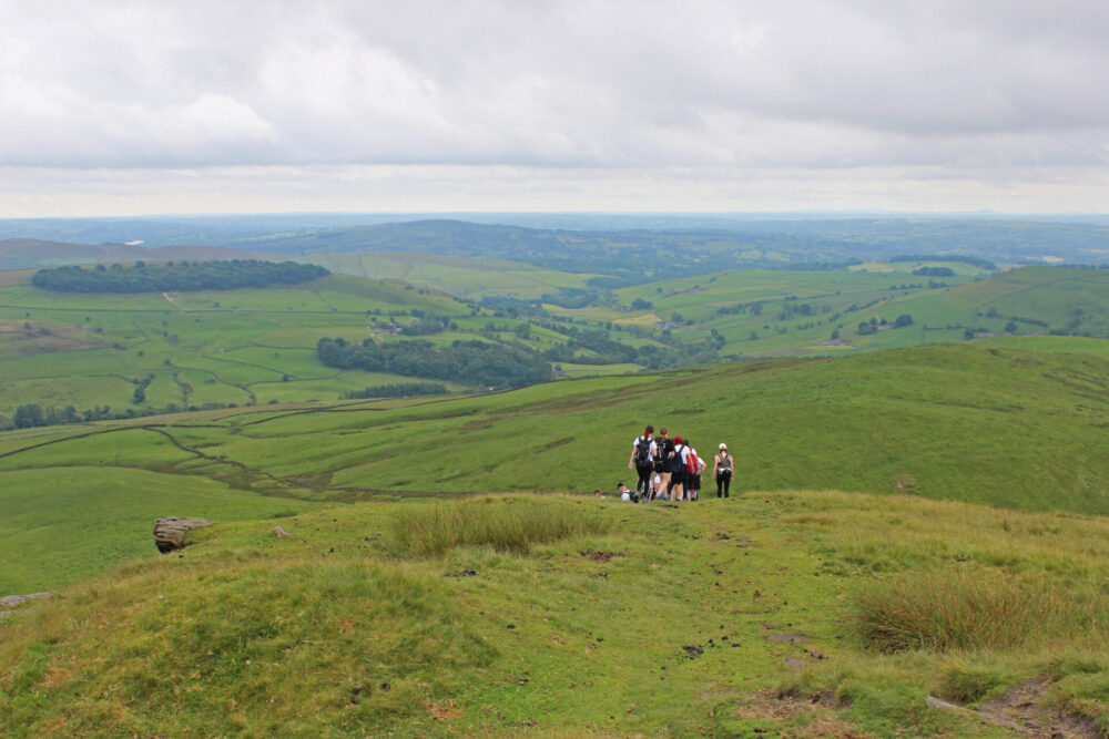 The back of a group of walkers can be seen from afar as they begin to descend the path form Shutlingsloe's peak