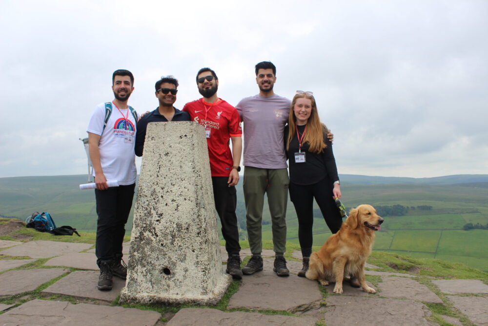 Four men, a woman and a pet dog pose at the trig point of Shutlingsloe