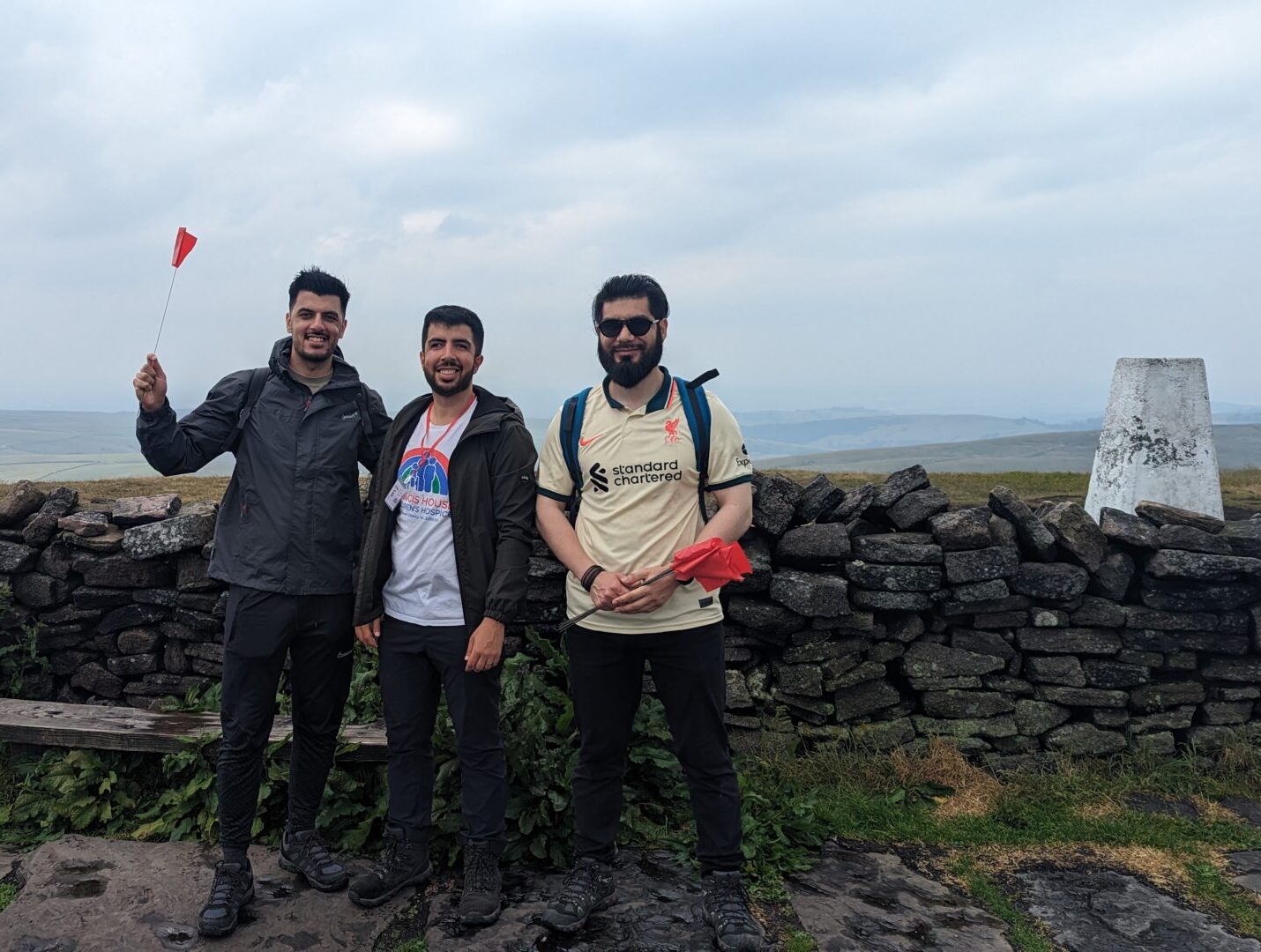 A group of three men holding flags stood on the top of a hill