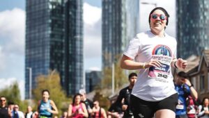 Women in Francis House T-shirt runs amongst crowd past Manchester skyscrapers