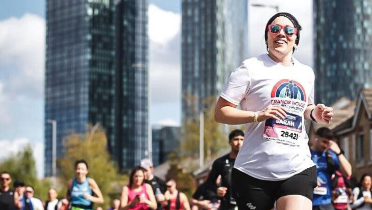 Women in Francis House T-shirt runs amongst crowd past Manchester skyscrapers