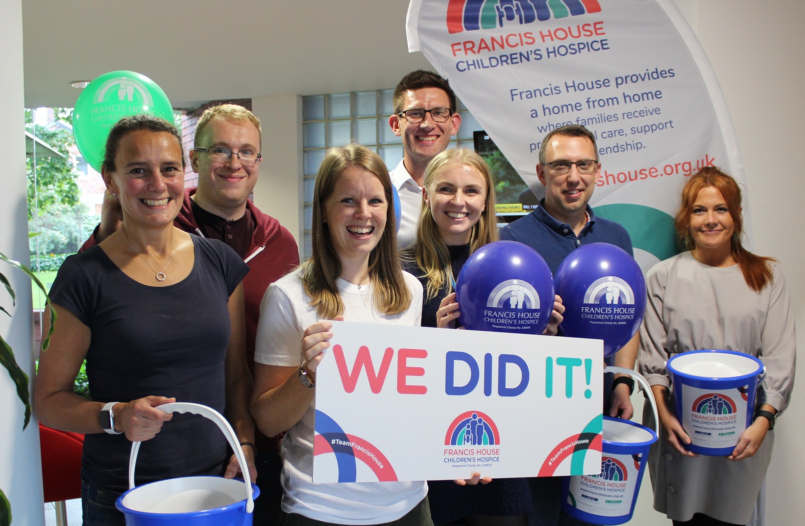 Group of people from Aquila Heywood holding Francis House charity balloons and banners