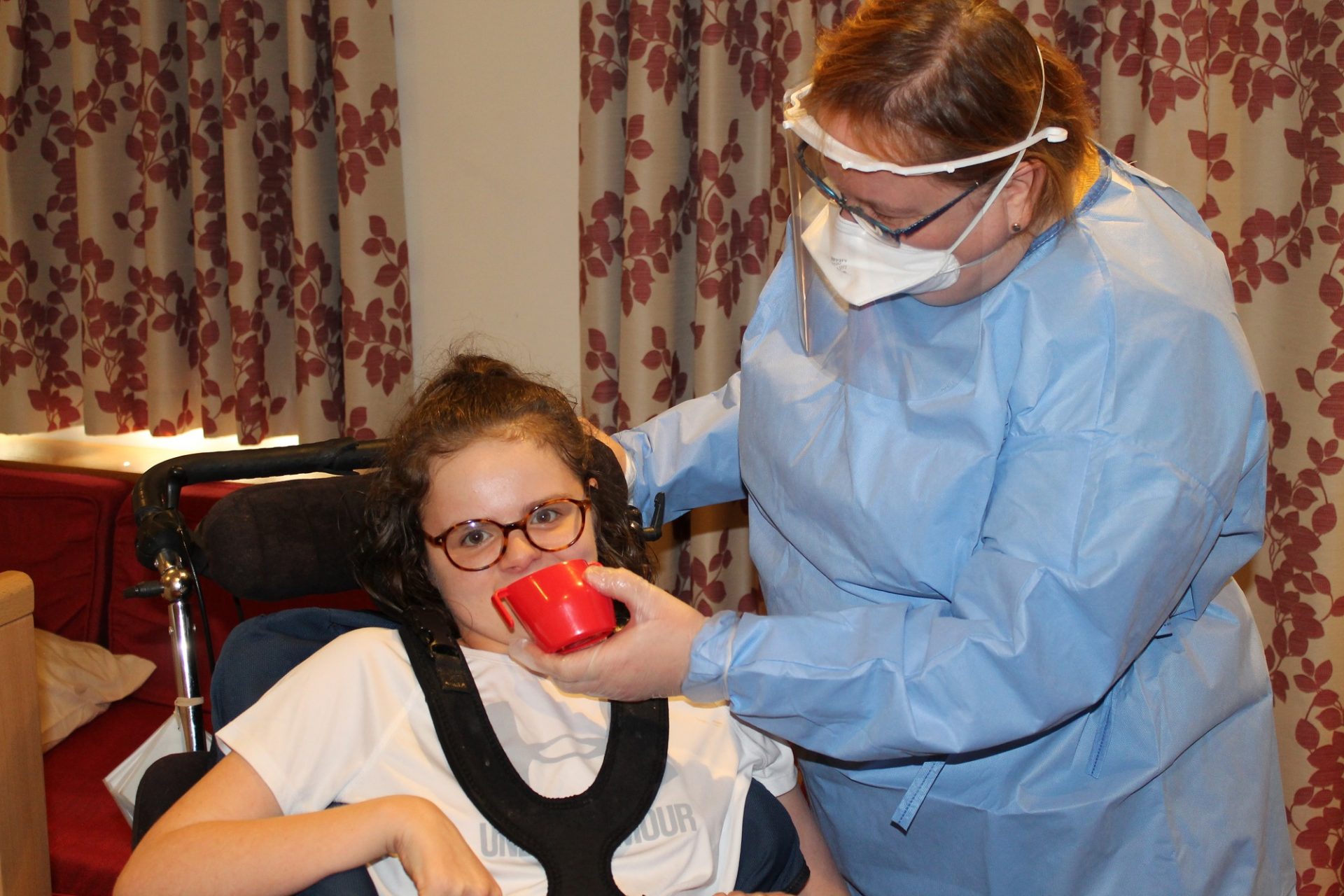 Child having a drink with care staff in PPE