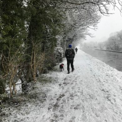 Man and dog wander down a snowy canal path