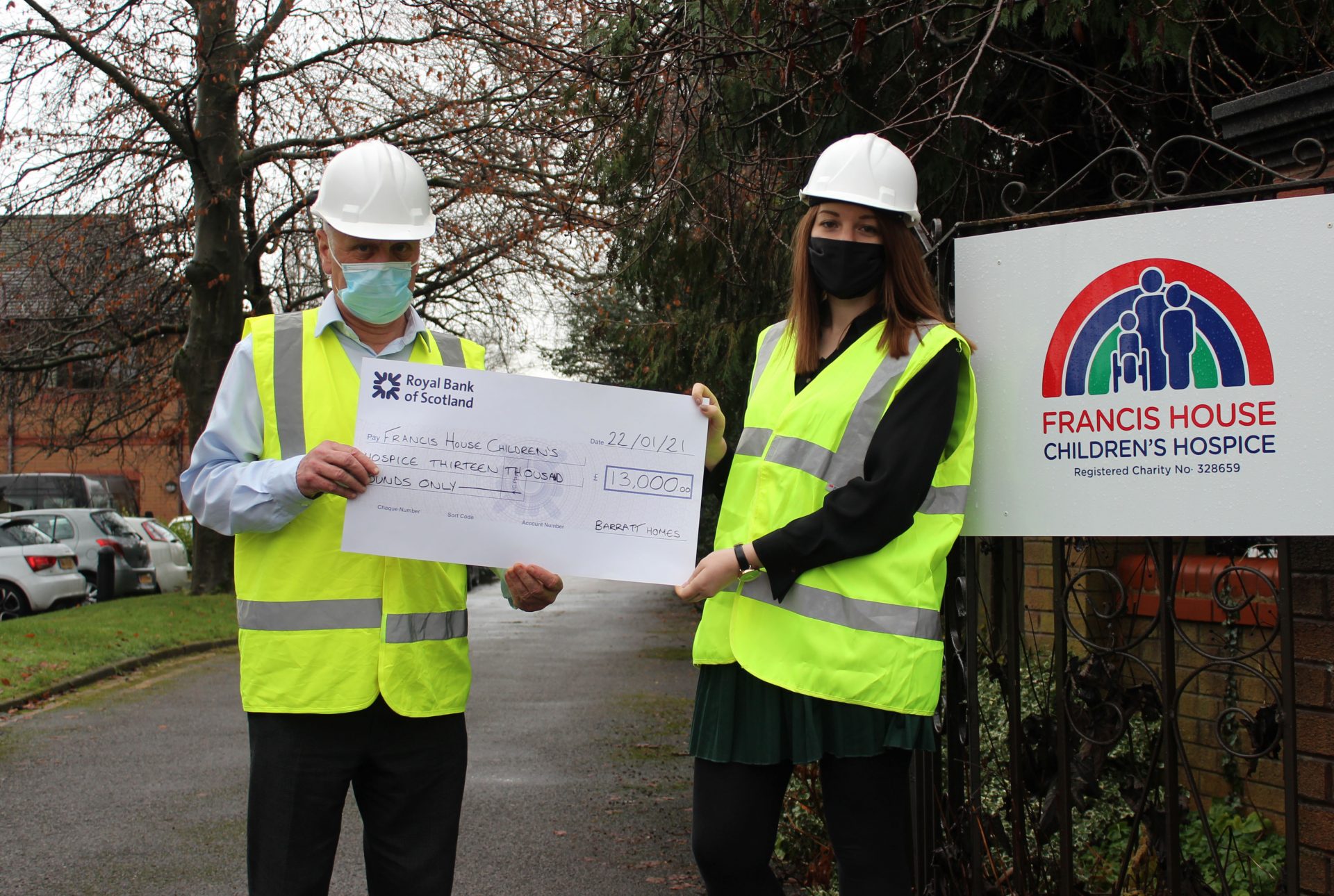 Two people wearing face coverings holding large cheque