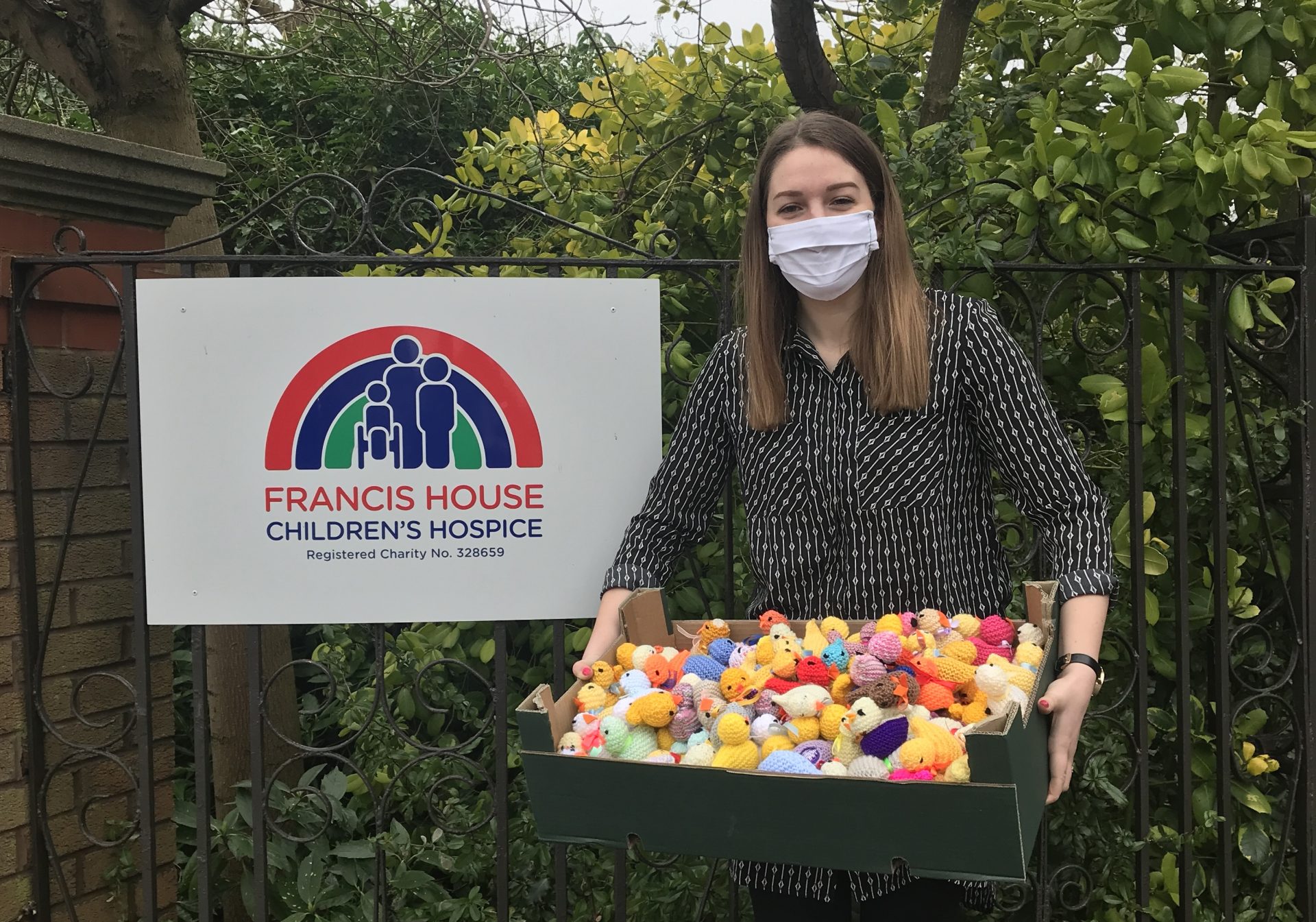 Woman wearing mask holding box of knitted chicks.