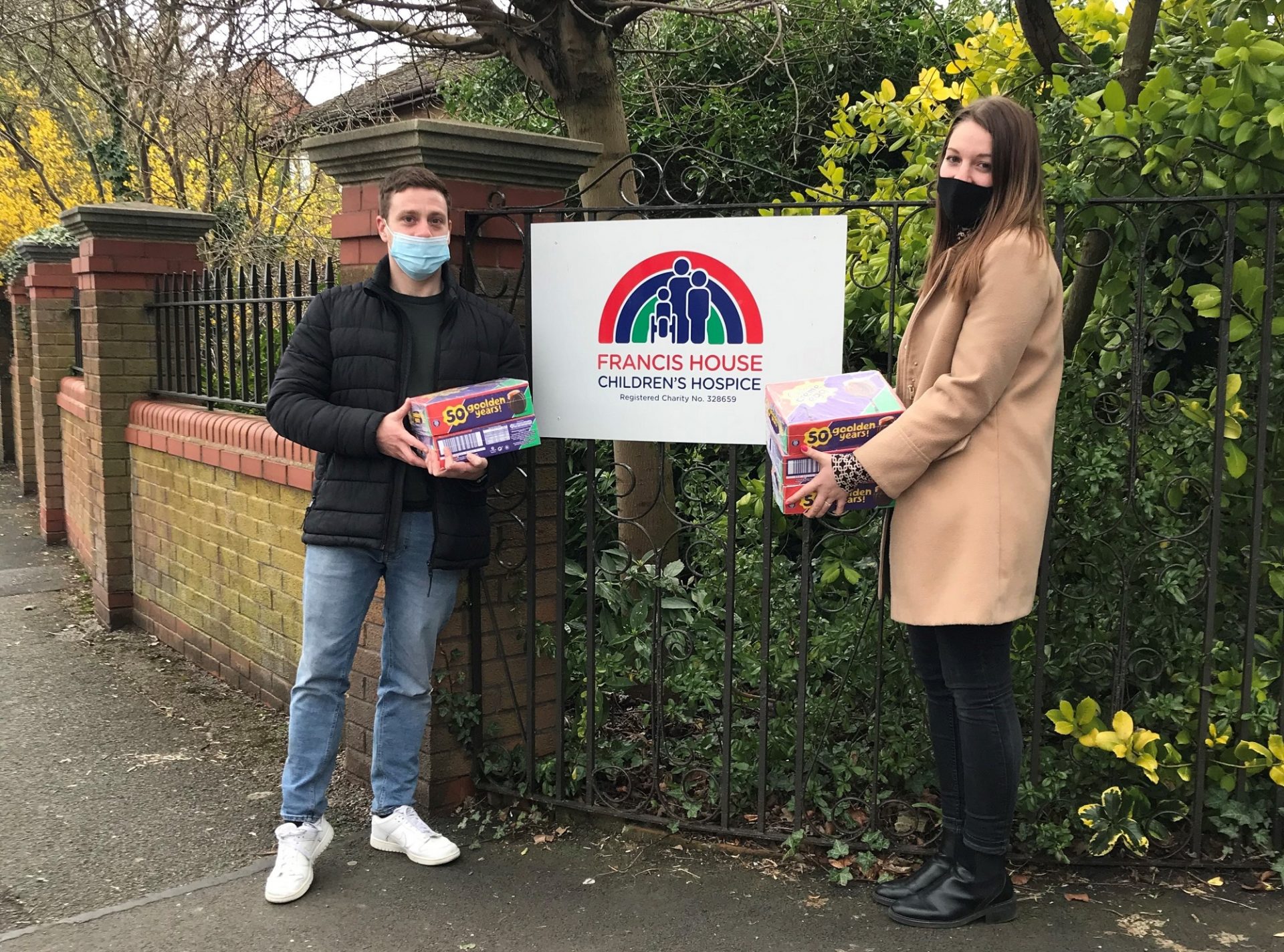 Two people holding boxes of creme eggs outside the gates of Francis House Children's Hospice