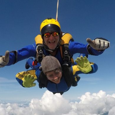 Lady skydiving with instructor showing thumbs up