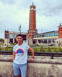 A man in a Francis House T-shirt stands in front of a wall with the Trafford Palazzo tower seen in the background