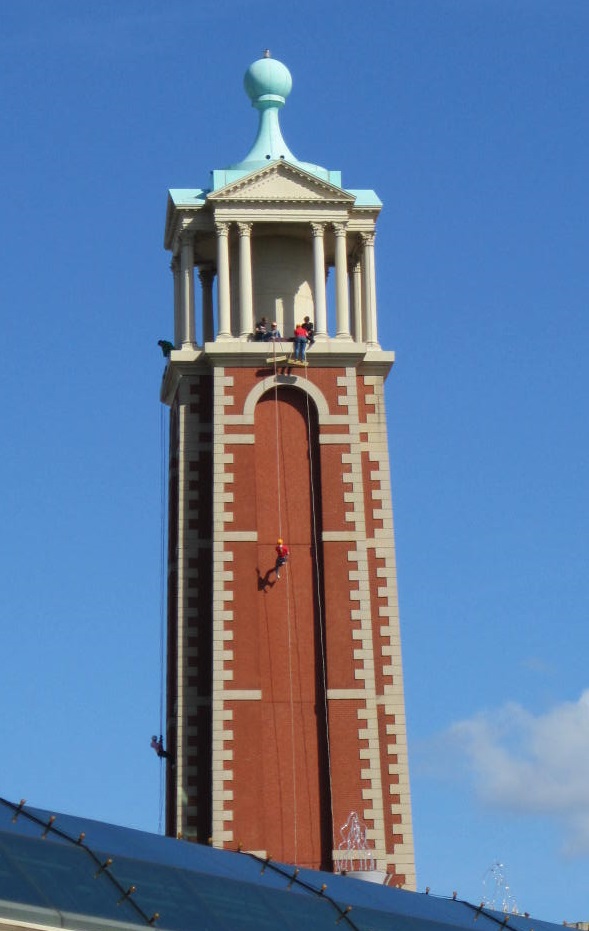 A view from the ground of the Trafford Palazzo Tower on a bright clear day, with an abseiling figure making their way down the side