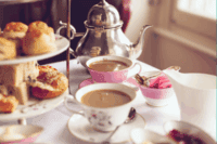 Table setting for afternoon tea with tea cups, scones and cakes