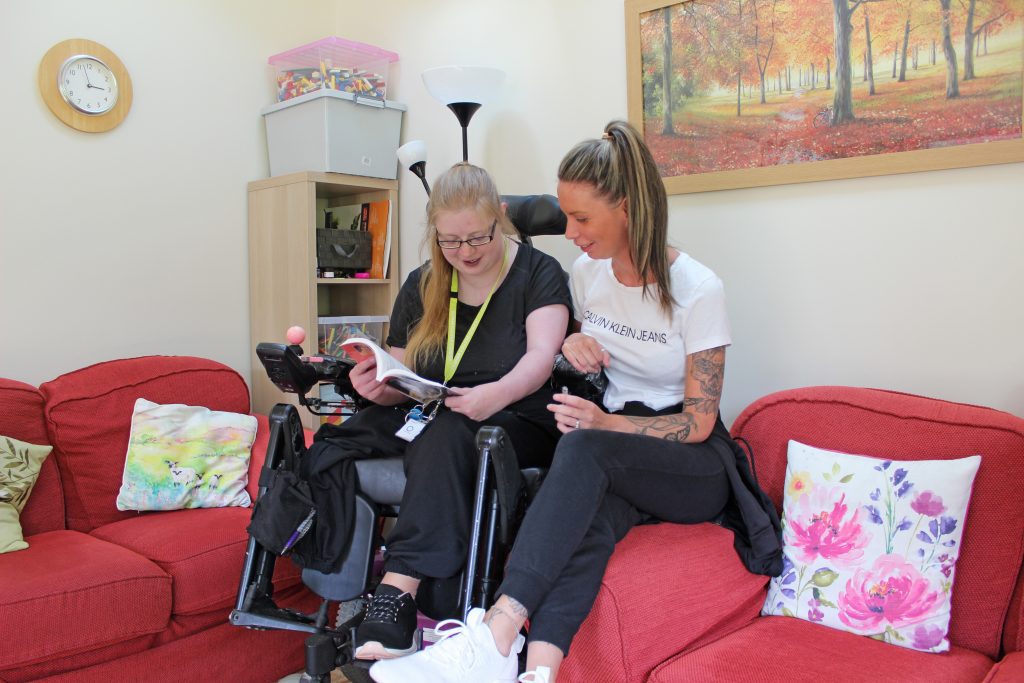 Young person in wheelchair reading a book with woman