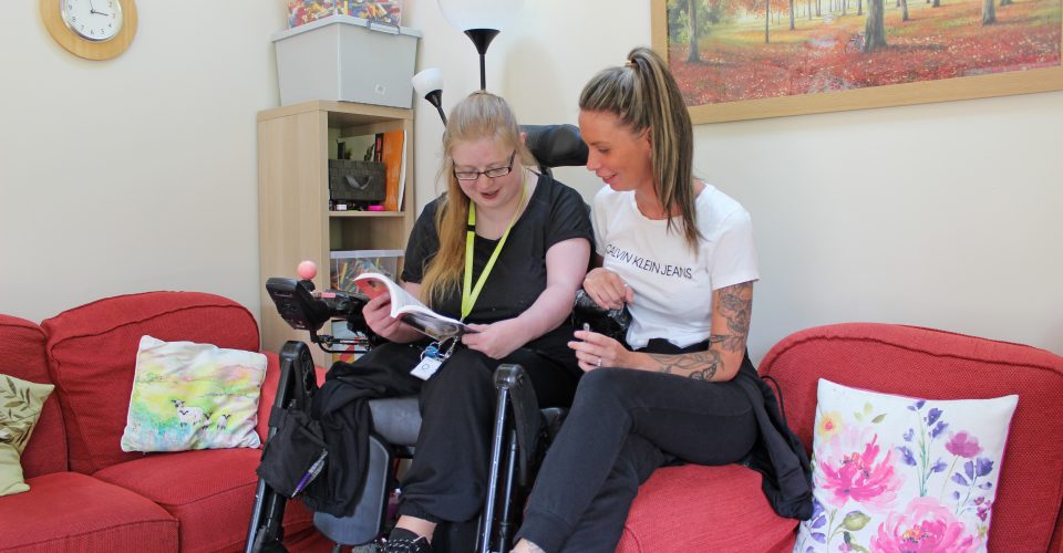 Young person in wheelchair reading a book with woman