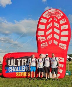 A group of four male participants in Francis house t-shirts stand beneath a giant inflatable boot print on the Ultra Challenge 2023