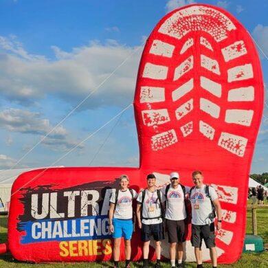 A group of four male participants in Francis house t-shirts stand beneath a giant inflatable boot print on the Ultra Challenge 2023