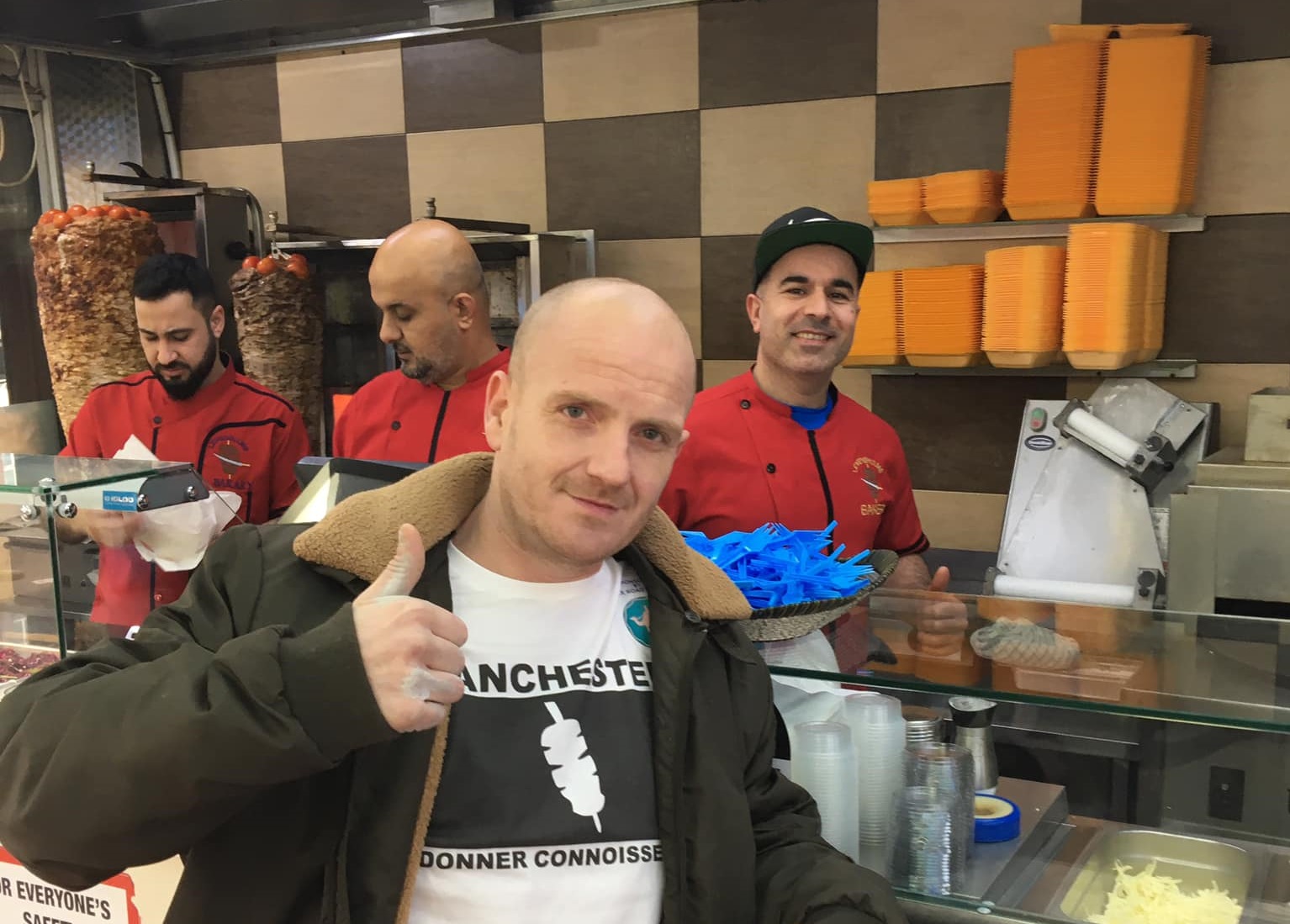 Man stood in kebab shop with smiling staff behind