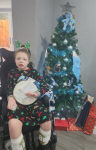 Child holding a drum sat in front of a Christmas tree