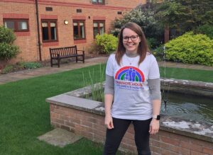 Woman stood in a courtyard by a fountain wearing a tshirt with a Francis House logo