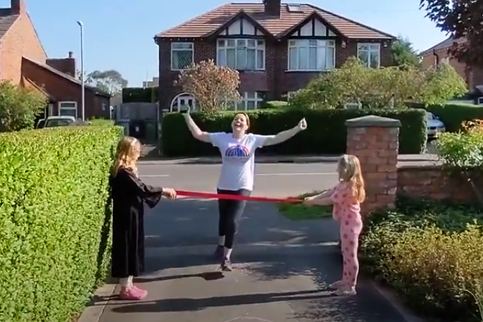 Woman with arms outstretched crosses a finish line held by two girls on a driveway