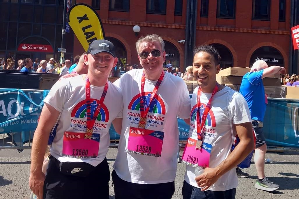 Three men wearing tshirts and medals stood on a street after a race