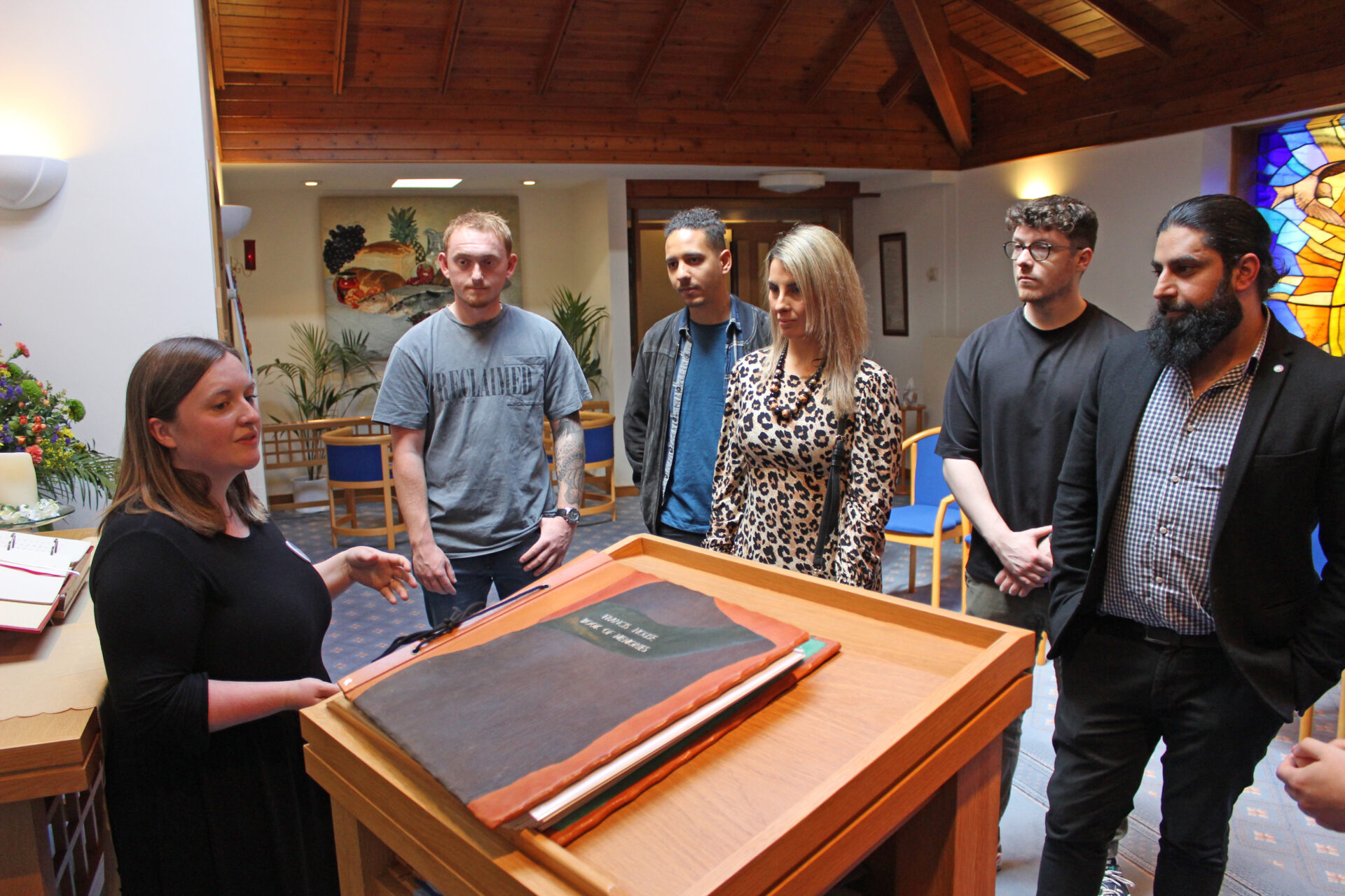 People stood listening to a woman talking stood by a book in a chapel