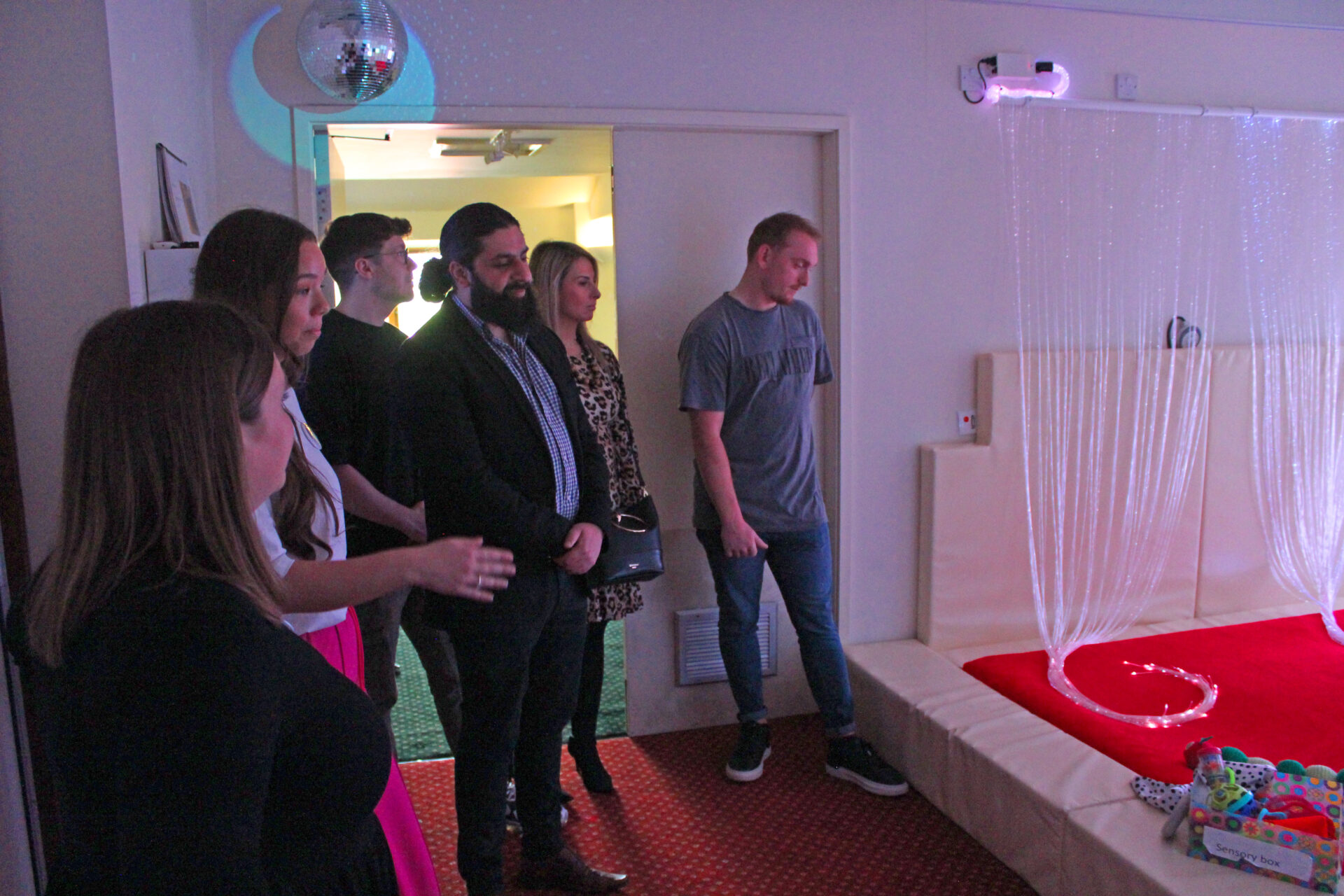 People looking at a sensory room with different coloured lighting