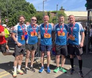 Five men wearing running vests and medals stood under a railway bridge