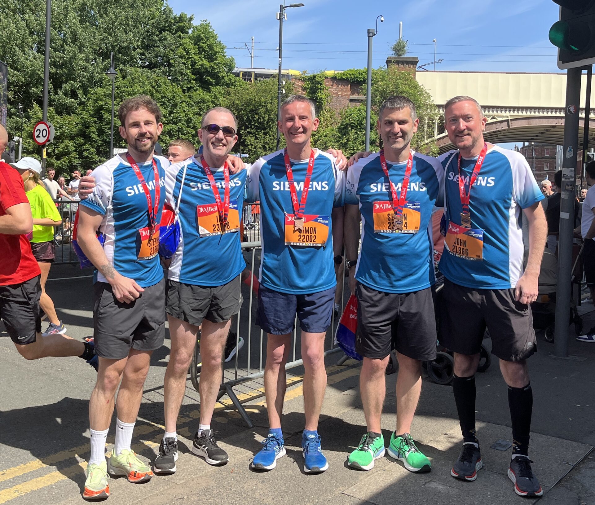 Five men wearing running vests and medals stood under a railway bridge