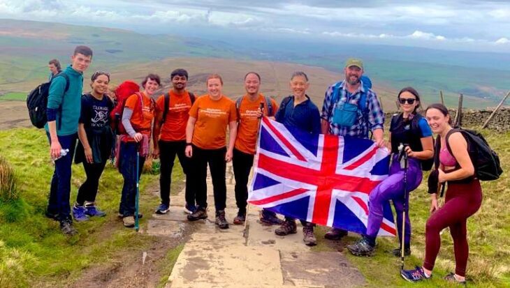 Group of hikers stood at the top of a hill in Yorkshire holding a large Union Jack flag