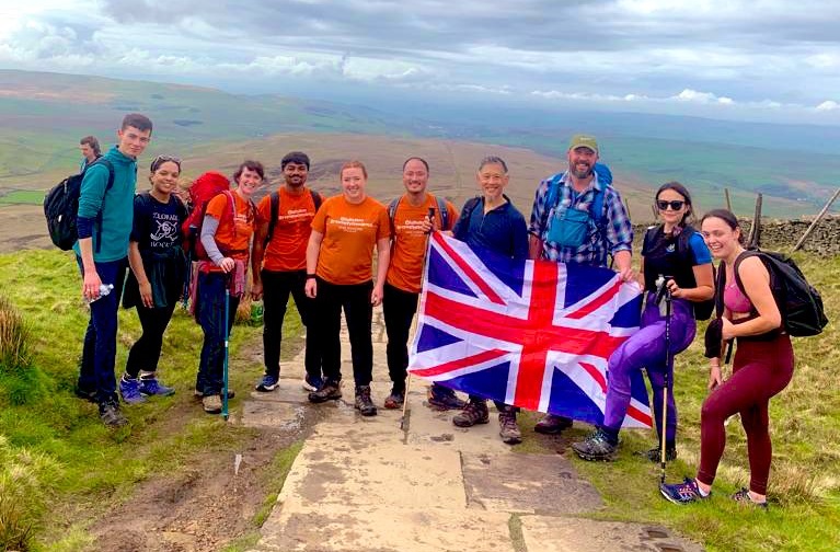 Group of hikers stood at the top of a hill in Yorkshire holding a large Union Jack flag