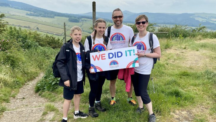 Two adults and two children stood in the countryside holding a sign with the words We Did It