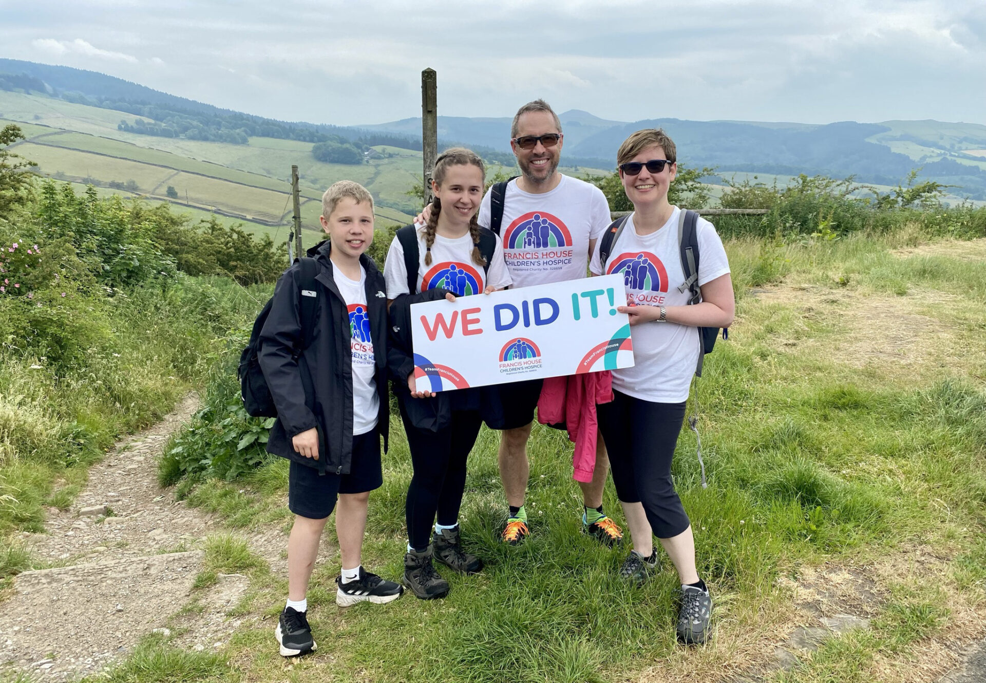 Two adults and two children stood in the countryside holding a sign with the words We Did It