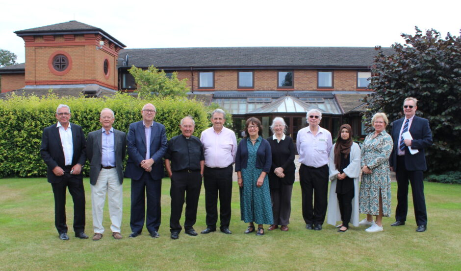 Group of people stood on a lawn infront of a brick building