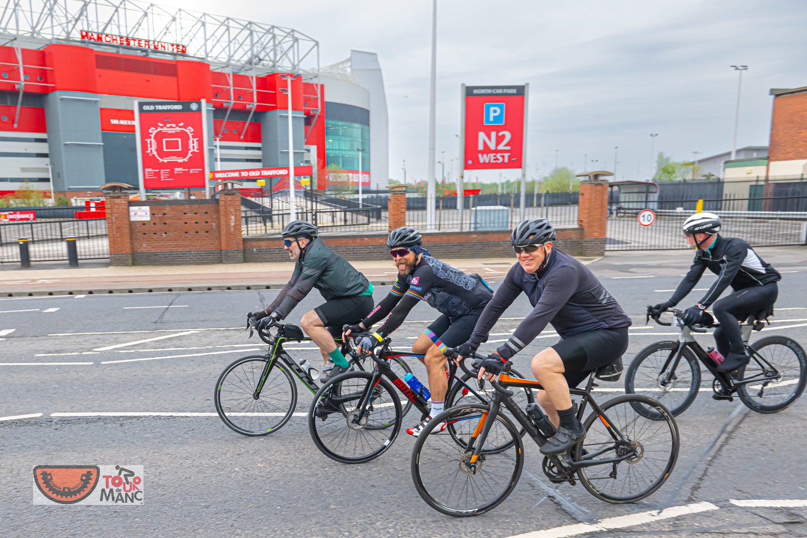 Four cyclists pass by Old Trafford along the Tour de Manc 2023