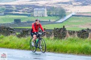 A cyclists smiles as she passes the camera whilst riding along Ashworth Rd on the 2023 Tour de Manc