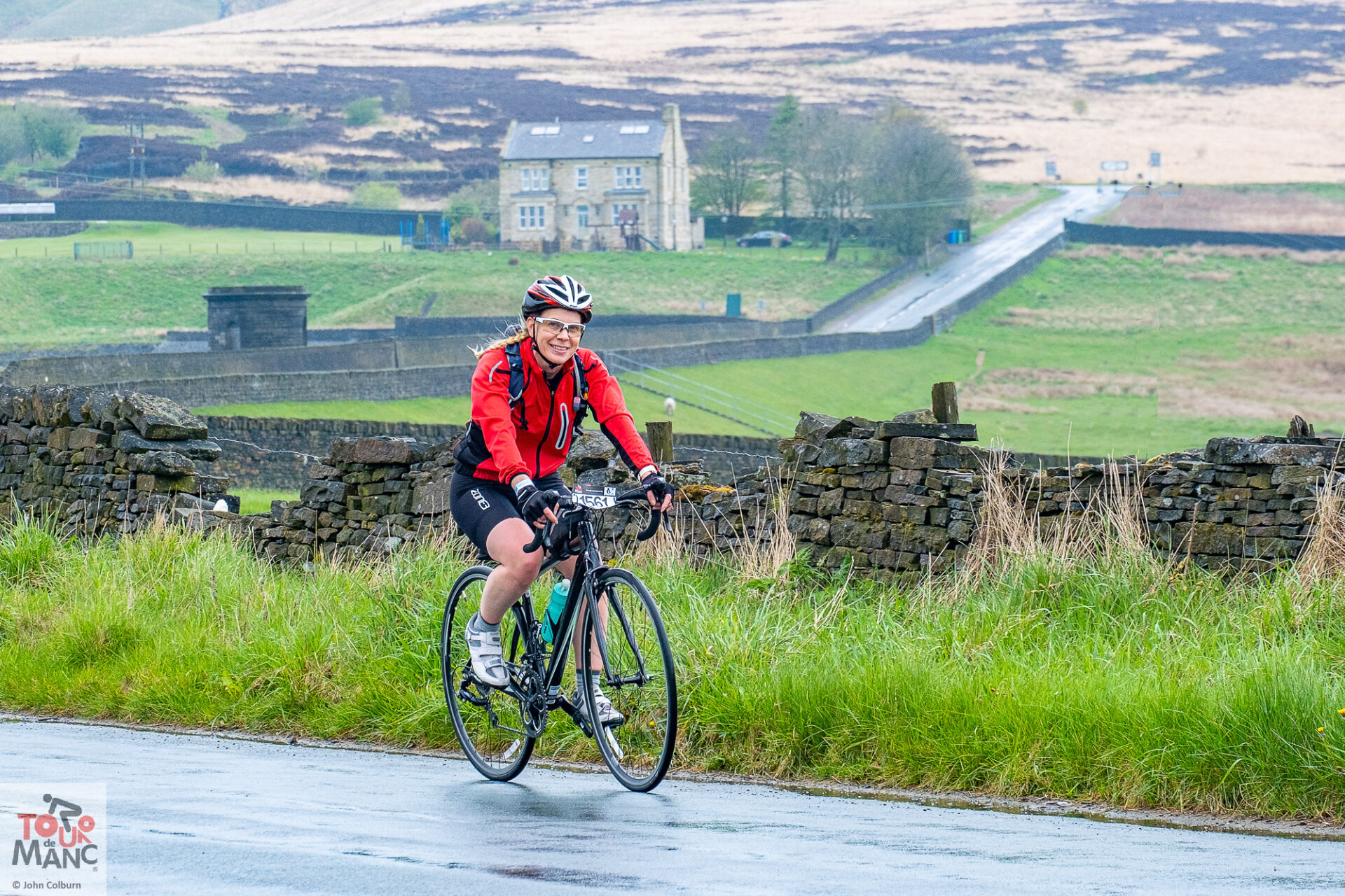 A cyclists smiles as she passes the camera whilst riding along Ashworth Rd on the 2023 Tour de Manc