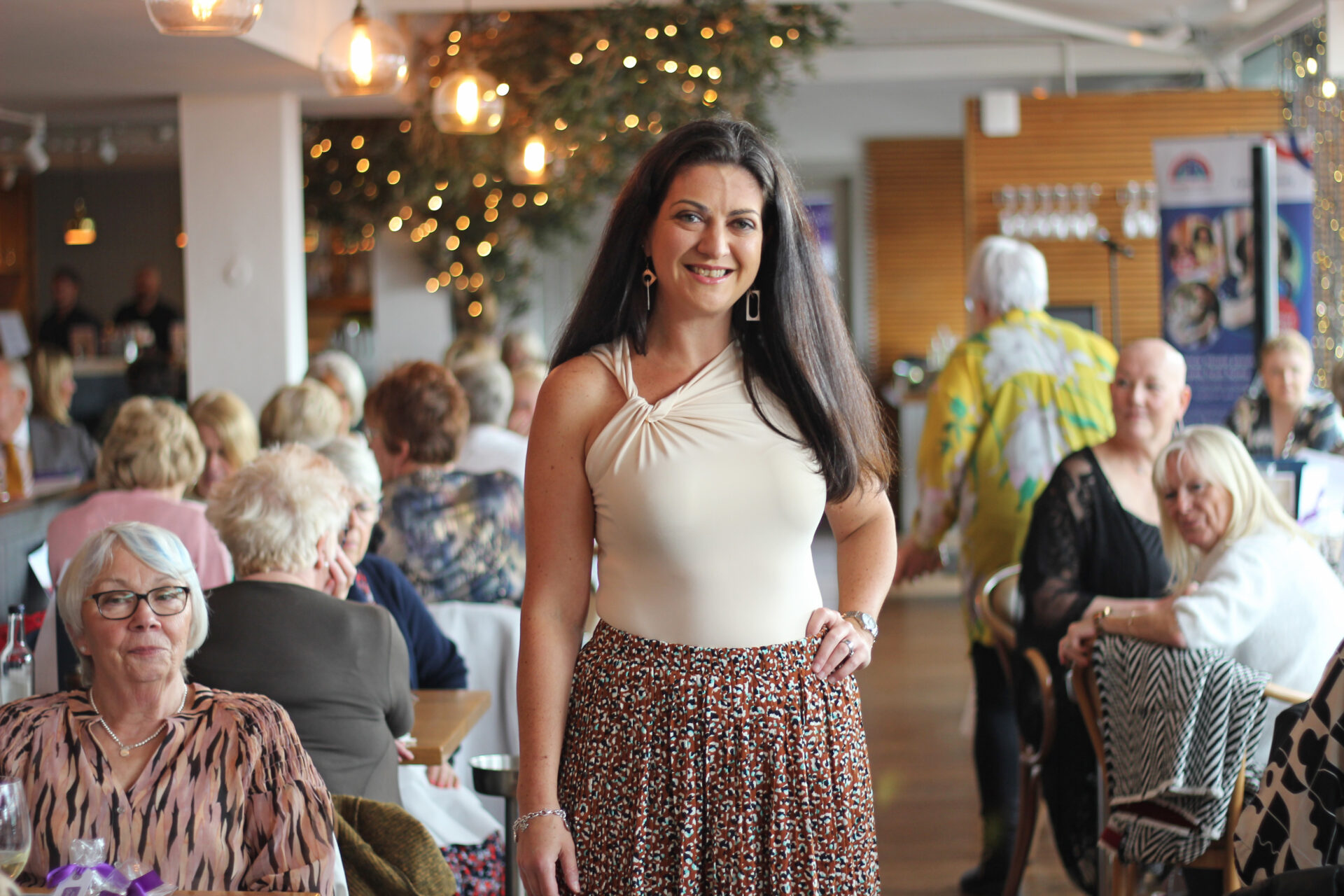 Woman wearing a cream top and brown skirt stood in a restaurant