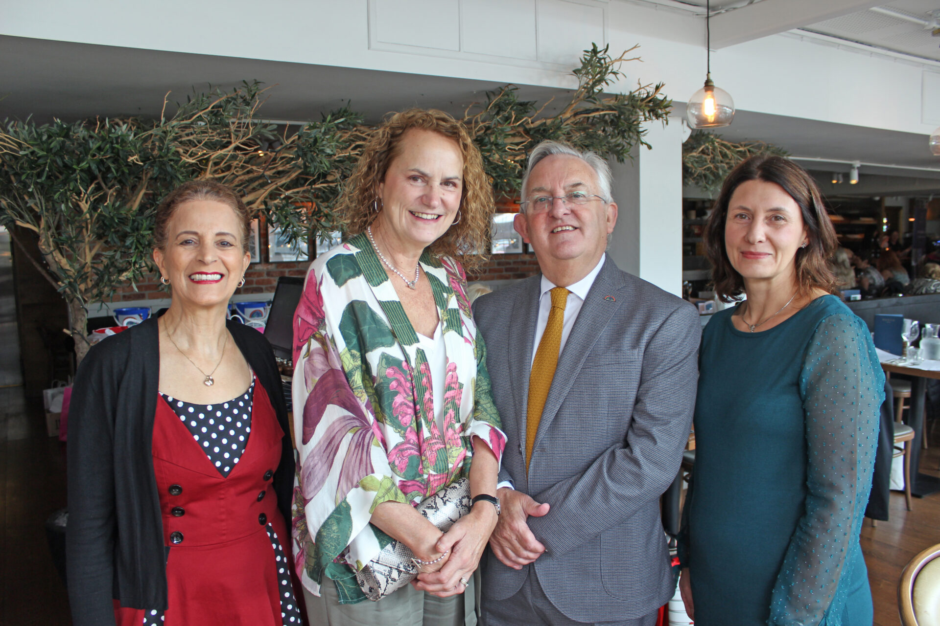 Three women and a man wearing smart clothing stood in a restaurant