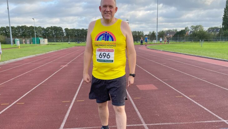Man wearing a yellow running vest standing on a running track