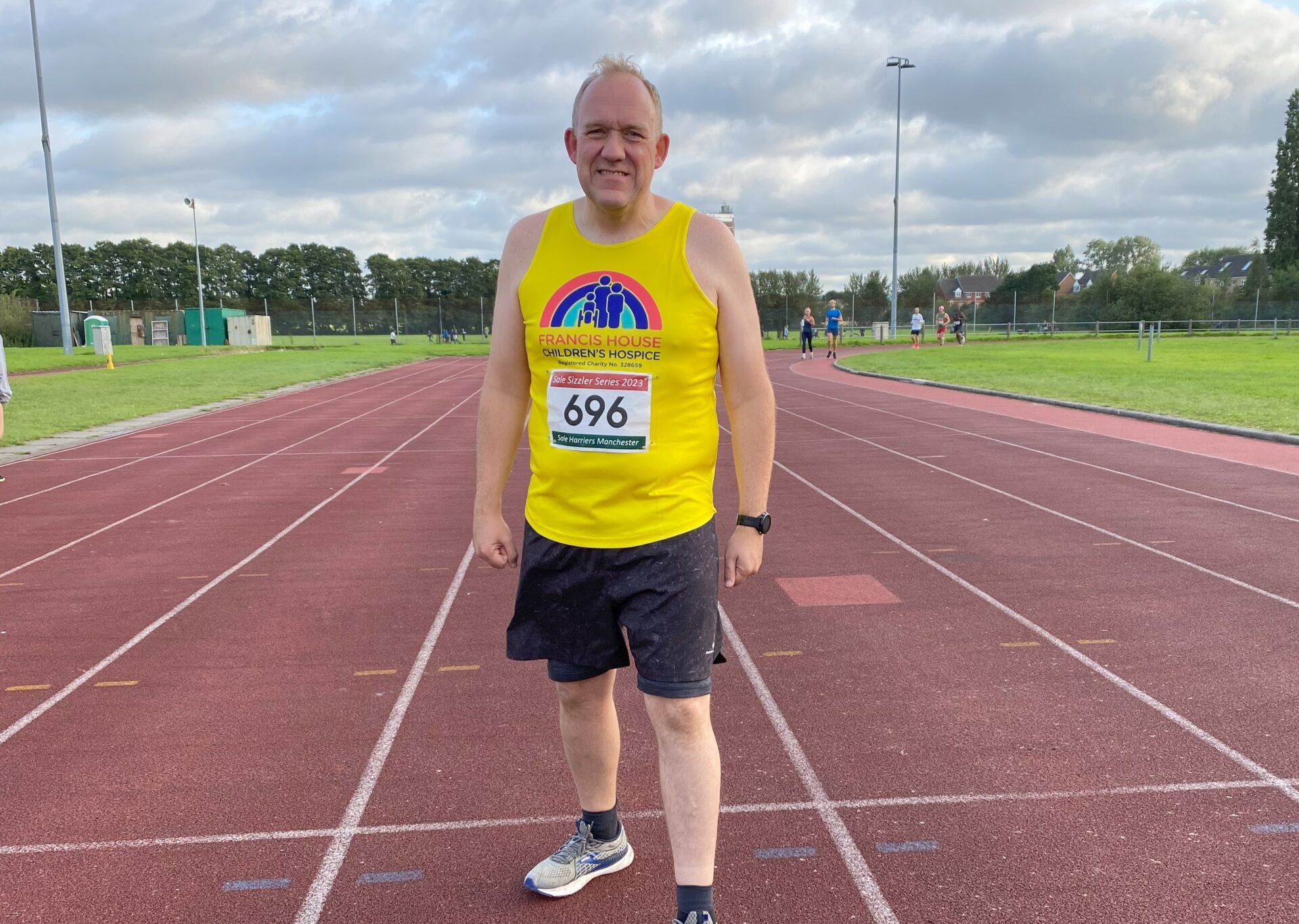 Man wearing a yellow running vest standing on a running track