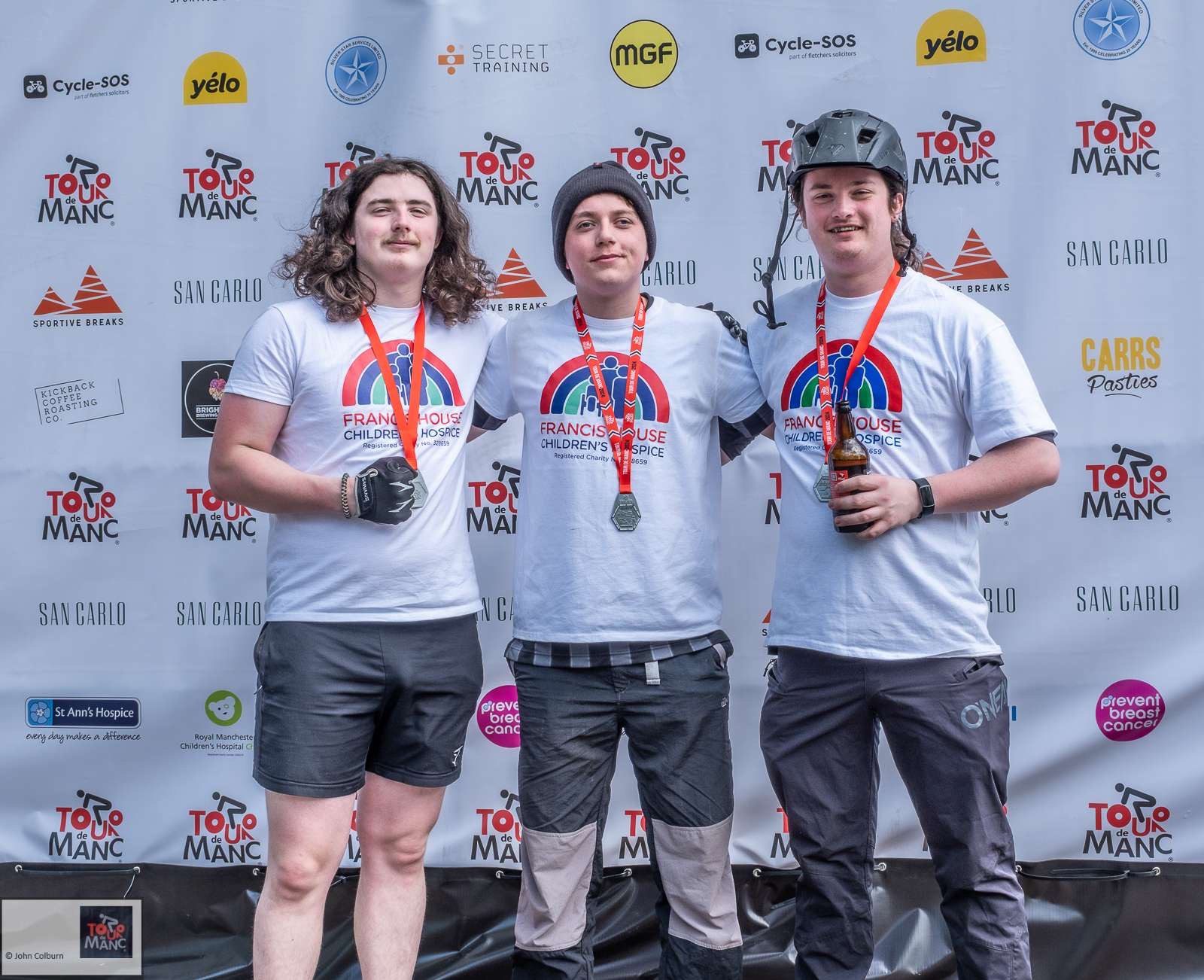 Participants of the 2024 Tour de Manc pose with their medals wearing Francis House T-shirts
