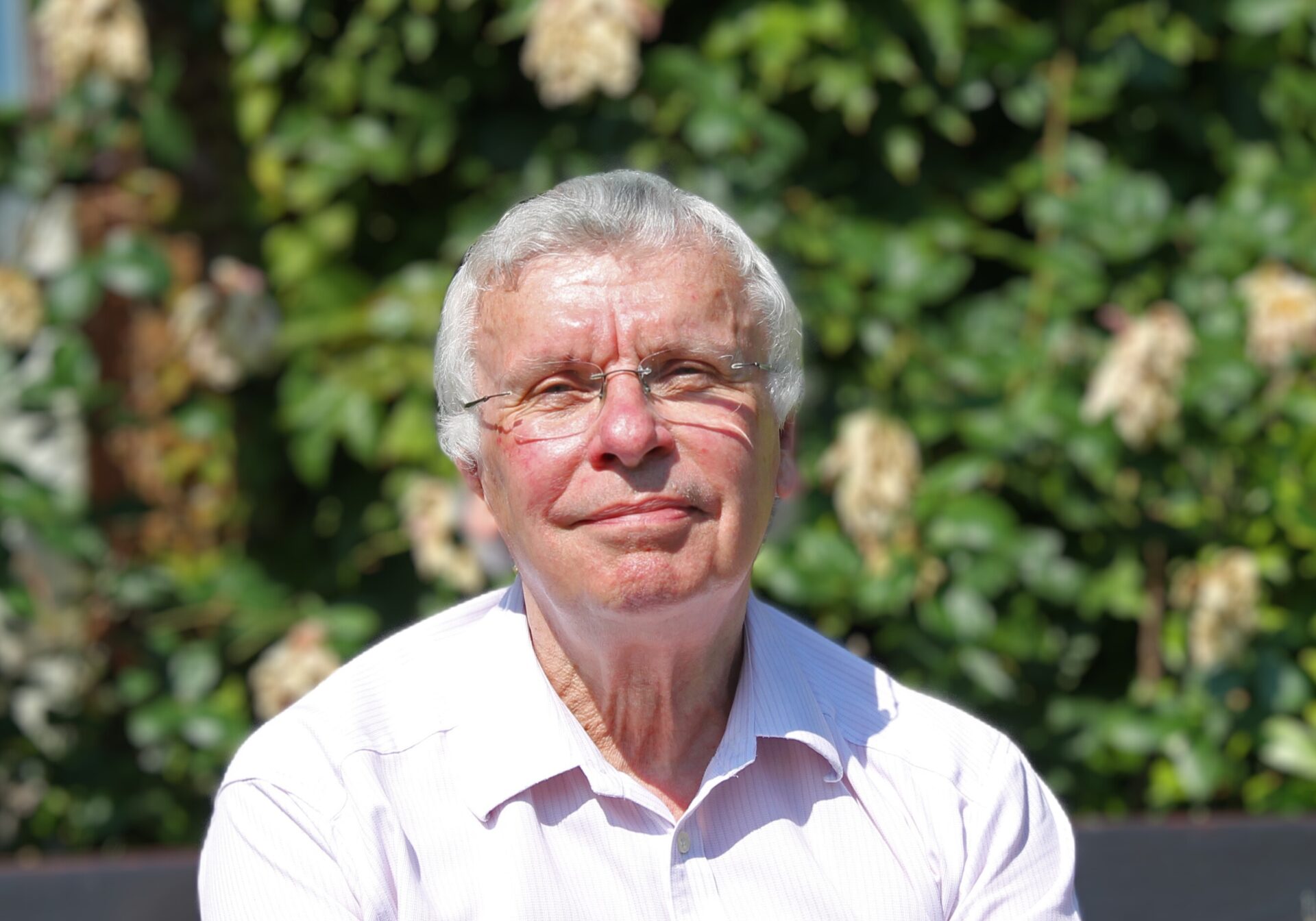 Man wearing a white shirt sat on a bench in front of a rose bush