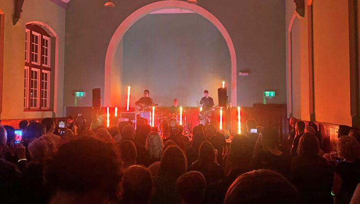 Three members of a band performing on a stage in front of a crowd