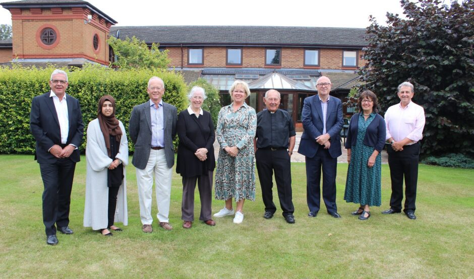 A row of people stood on a lawn infront of a brick building