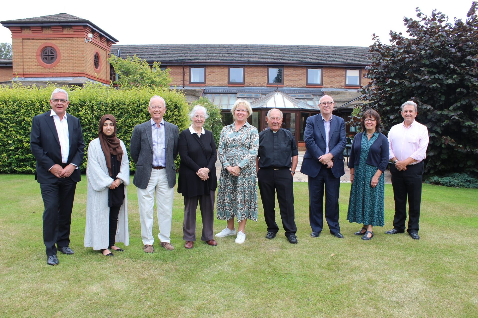 A row of people stood on a lawn infront of a brick building