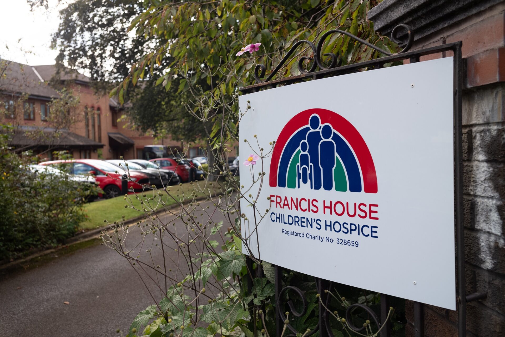 Entrance gates with Francis House signage and building and carpark in the background