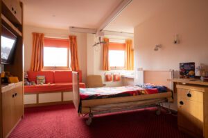 Child hospice bedroom with orange walls, curtains and bedspread.