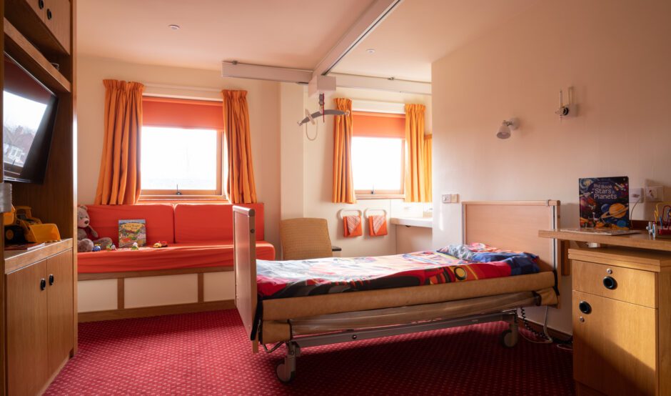 Child hospice bedroom with orange walls, curtains and bedspread.