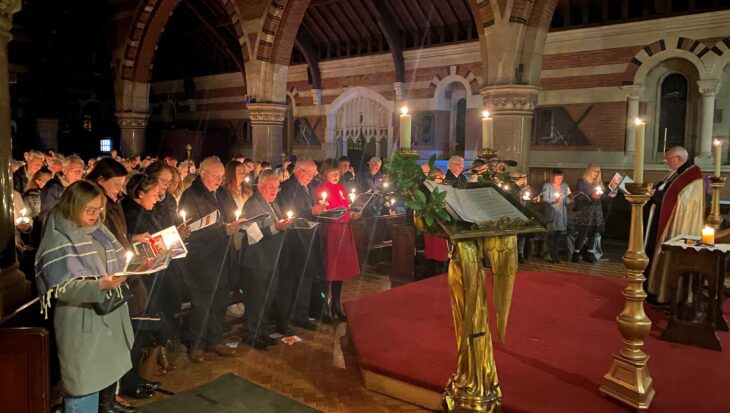 People holding candles and hymn sheets singing in a church